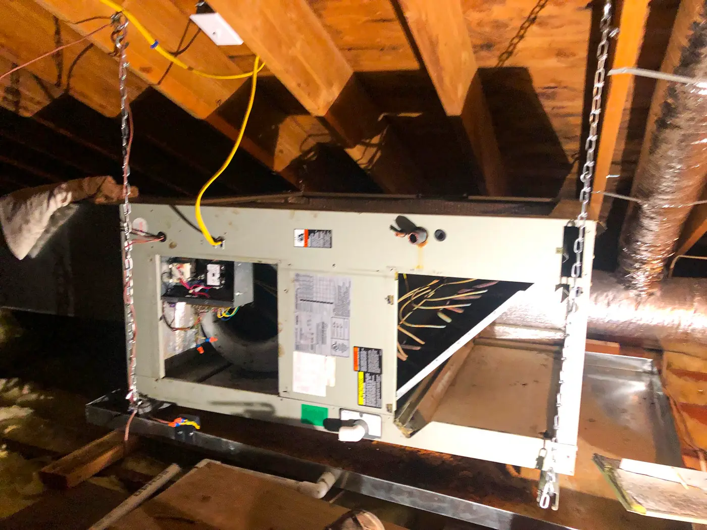 Air handler suspended on chains between attic rafters with wiring attached