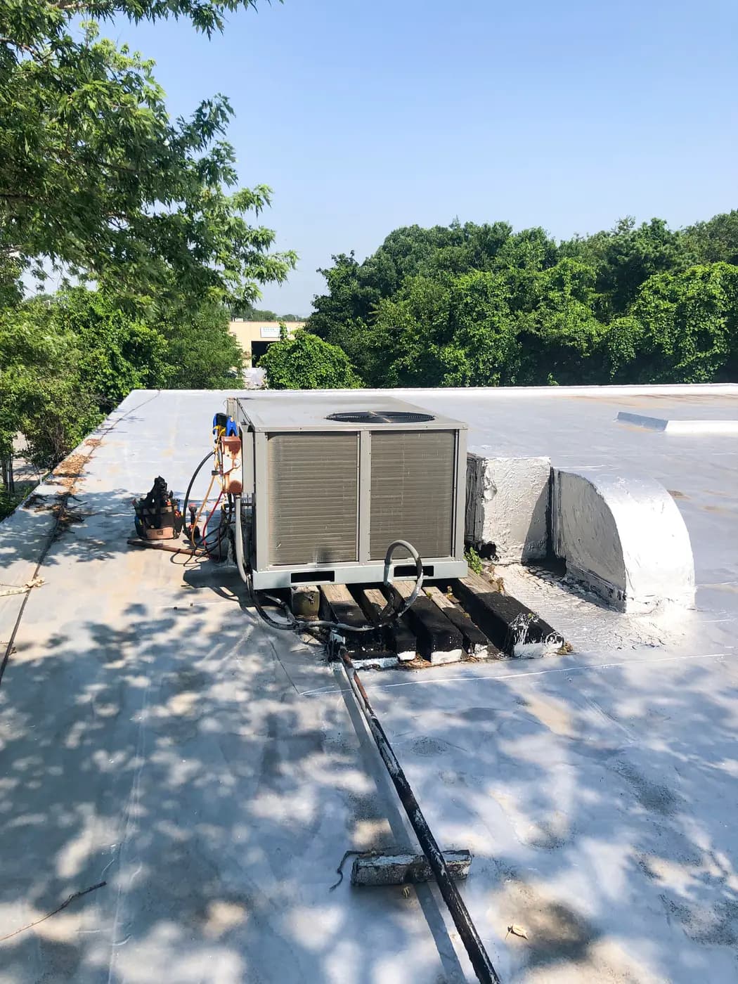 Condensing unit on flat commercial roof with line set running along deck