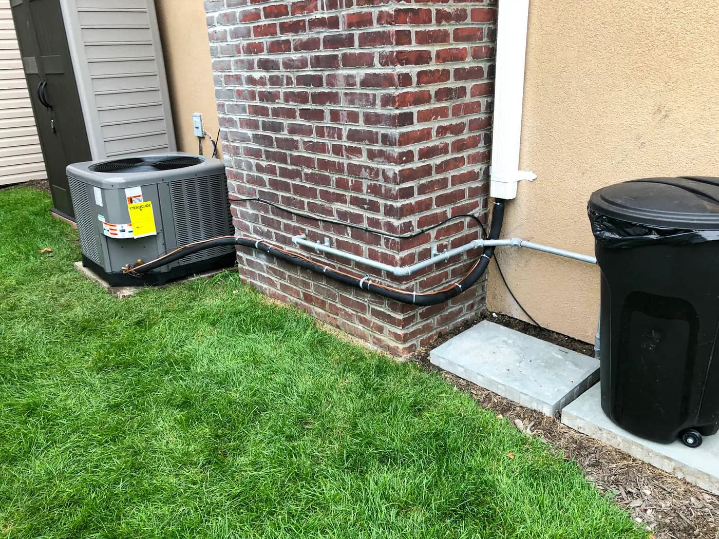 Outdoor condenser on pad beside brick and stucco home on lawn