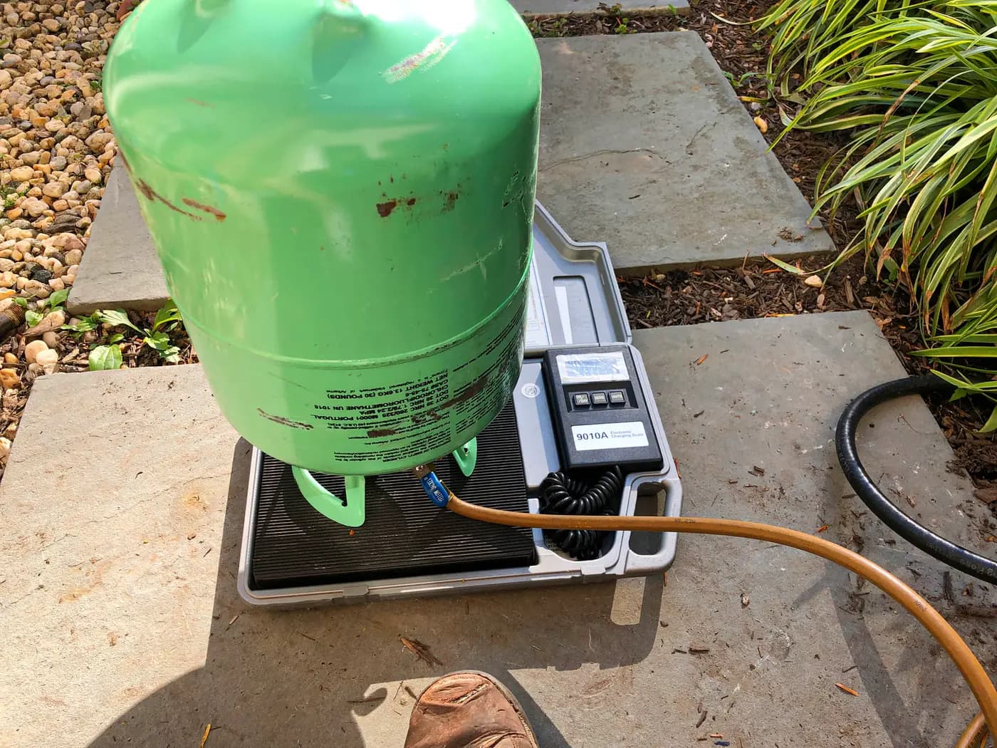 Green refrigerant recovery tank sitting on digital charging scale outdoors