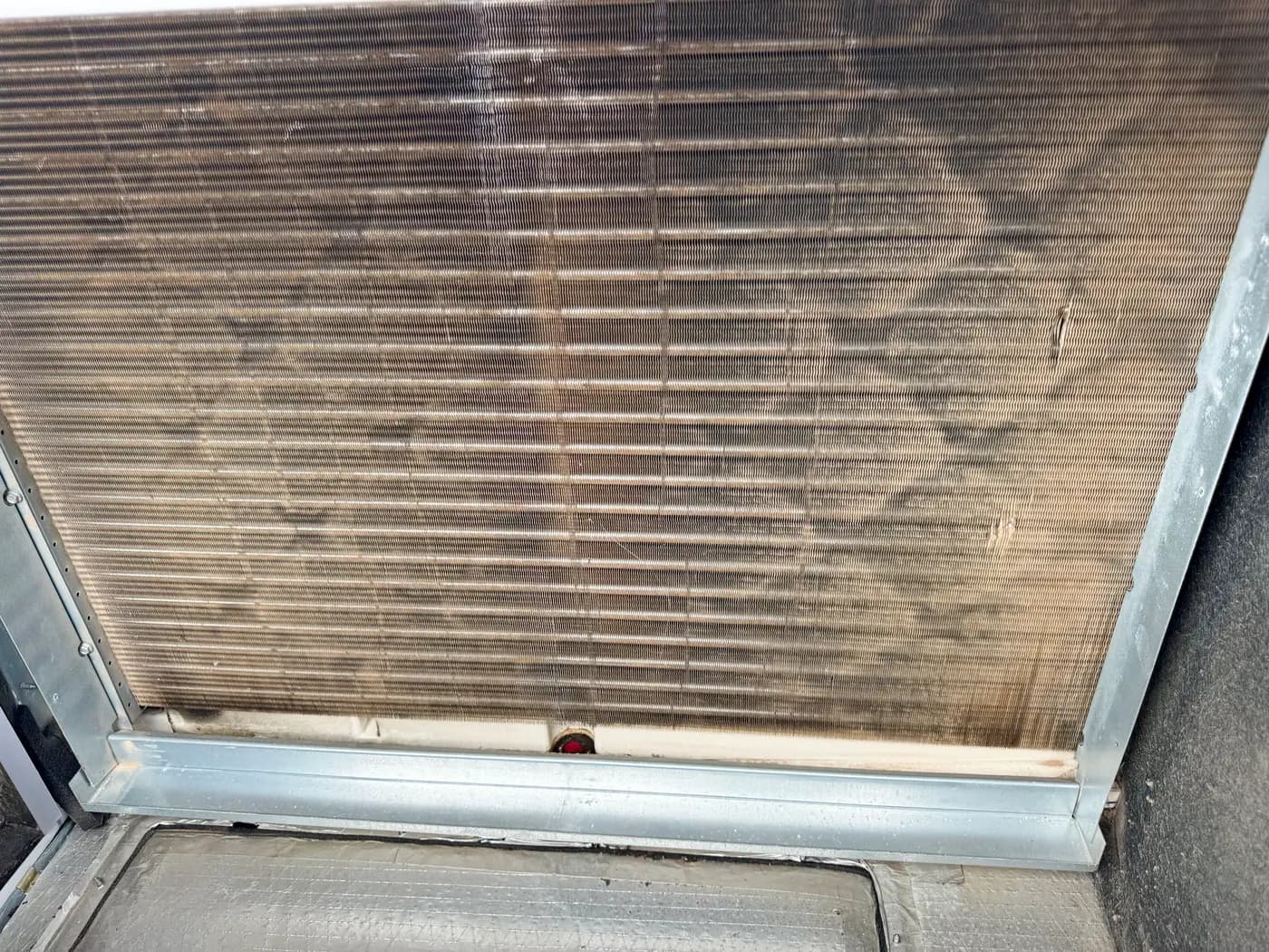 Close-up of soiled evaporator coil fins inside sheet metal cabinet
