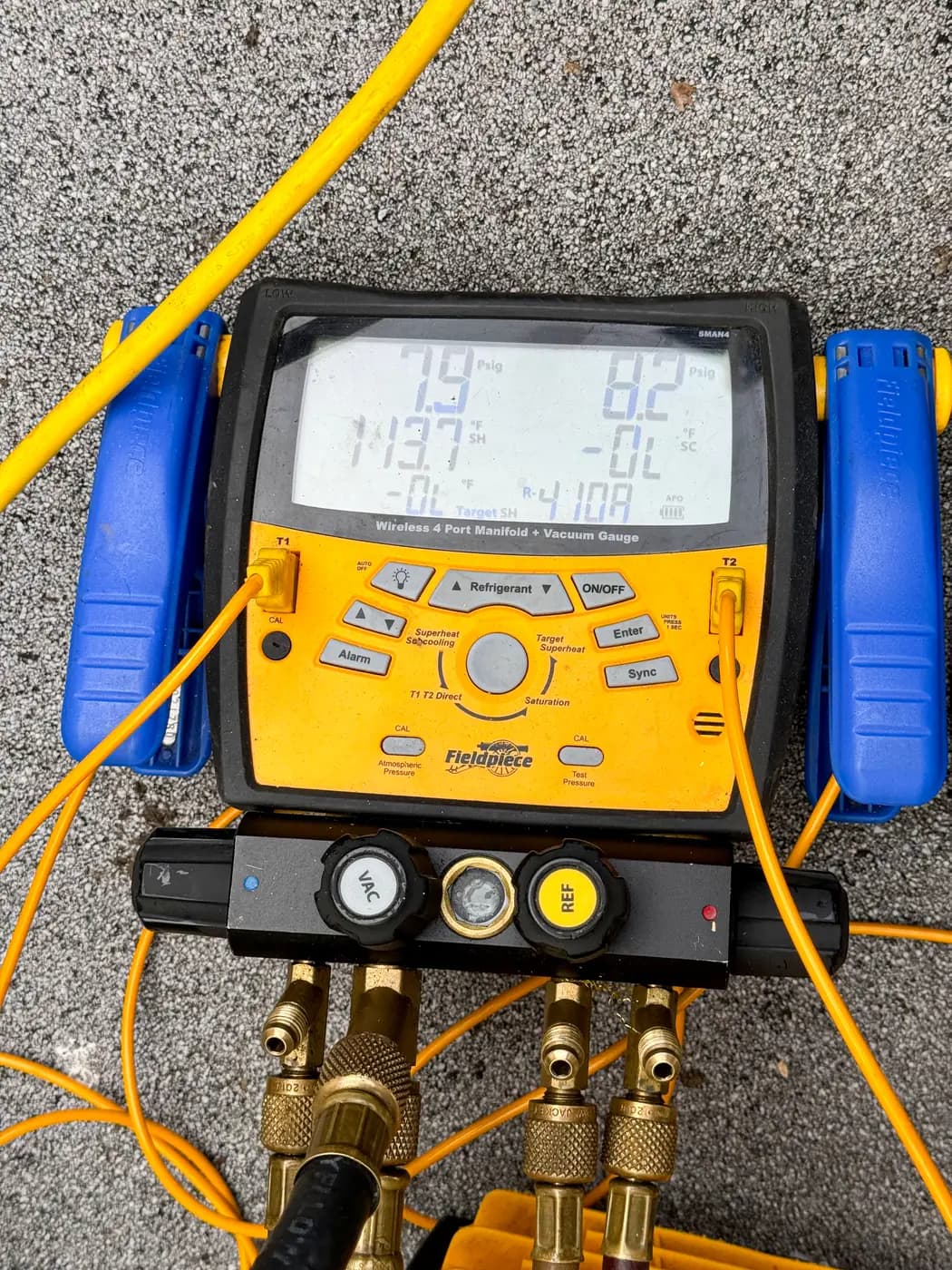 Digital refrigerant manifold gauge set with yellow hoses on pavement