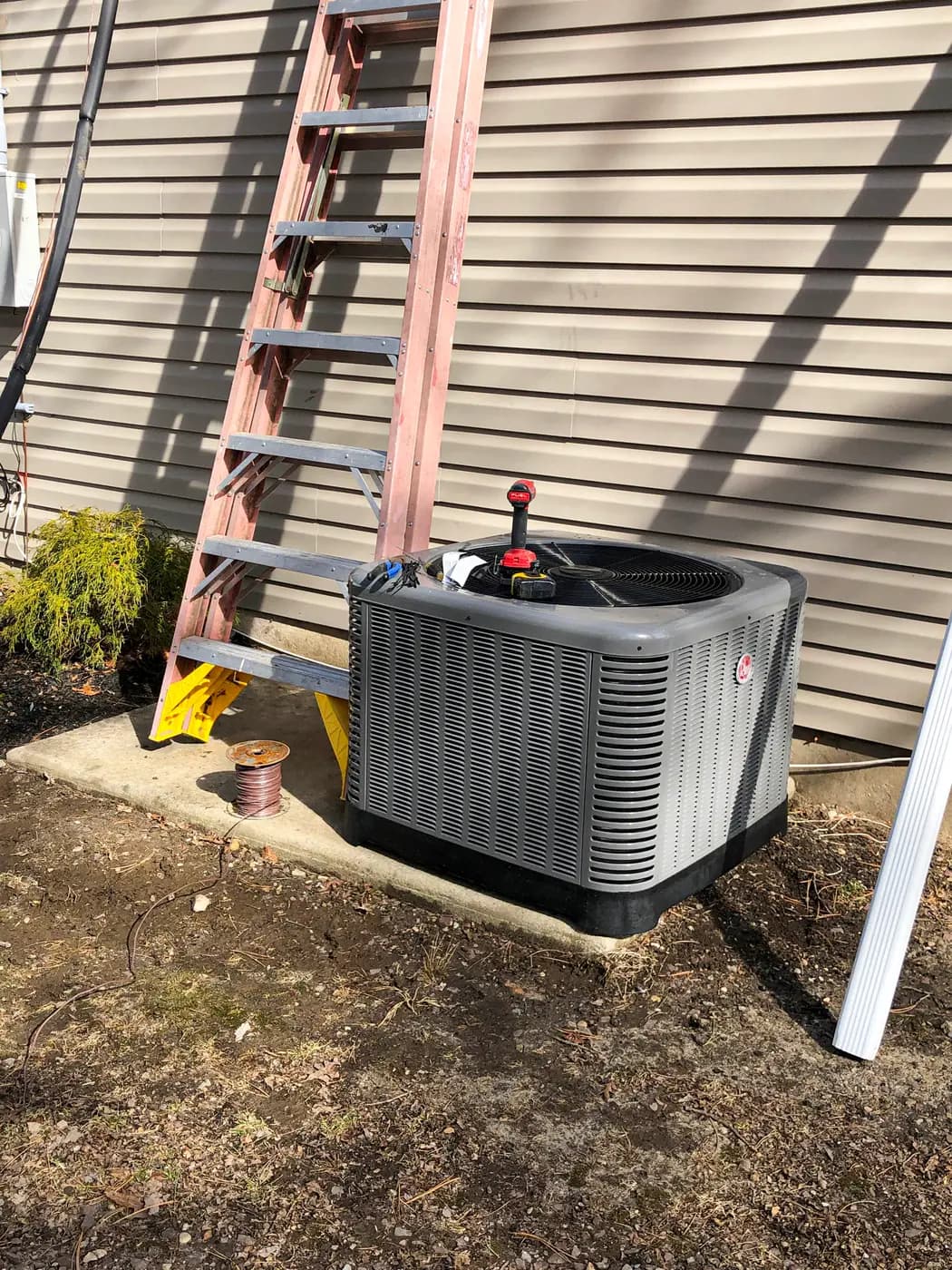 Rheem condenser on concrete pad against siding with ladder leaning above