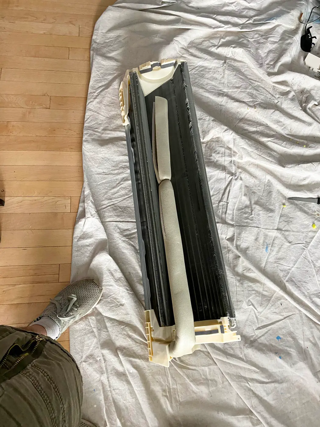 Ductless mini split indoor unit laid on drop cloth over wood floor