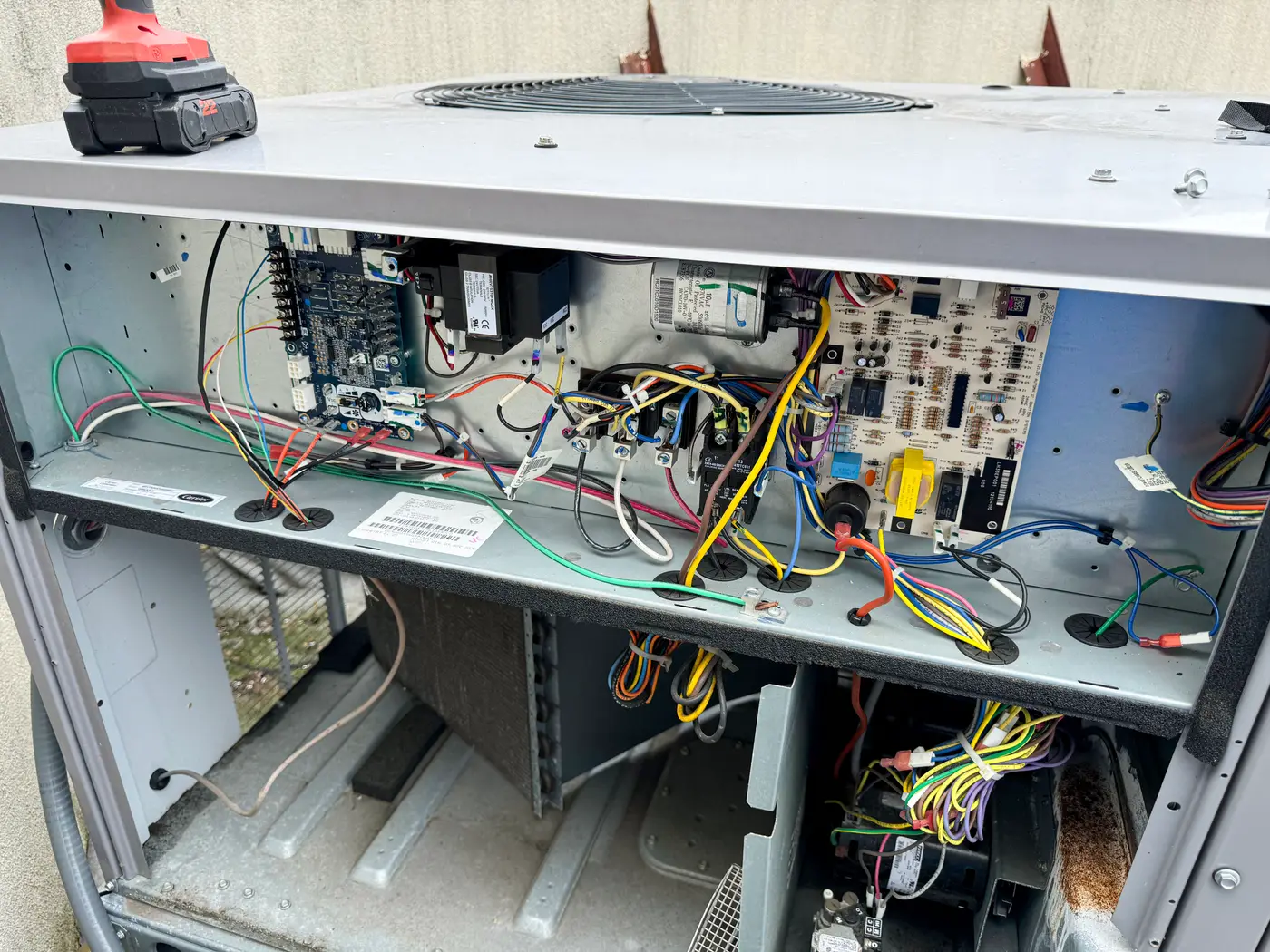 Open rooftop unit control compartment with wiring harnesses and drill on top