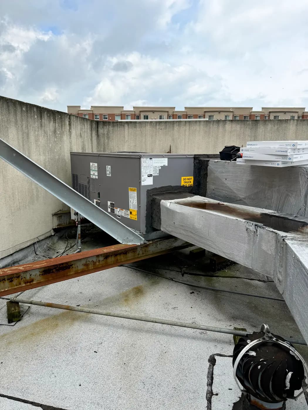 Rooftop unit beside steel beam and duct chase on weathered roof