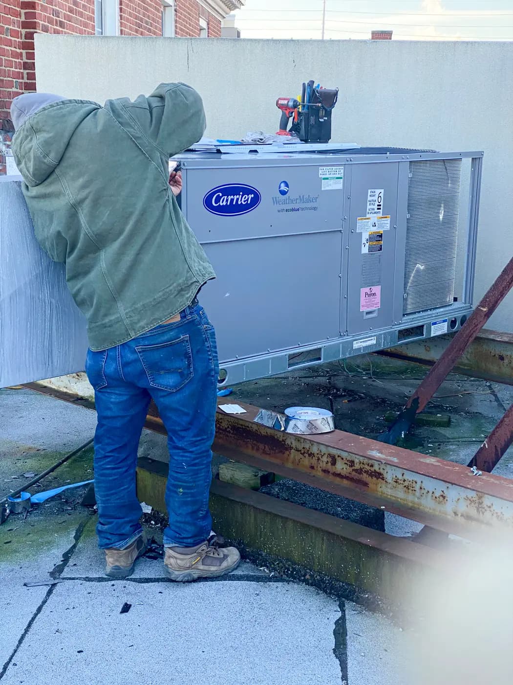 Technician in hooded sweatshirt working on Carrier rooftop unit