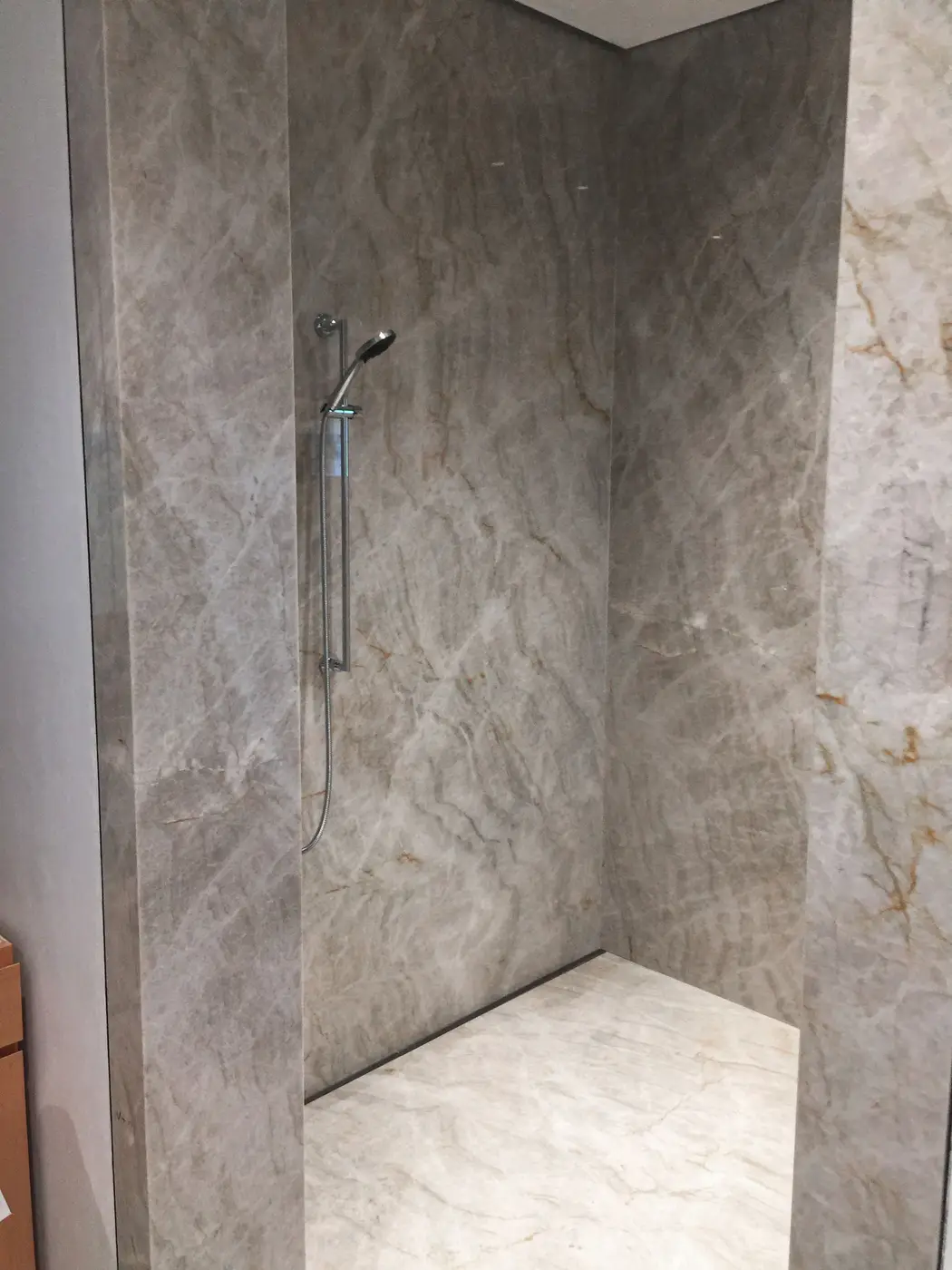 Finished walk-in shower with large marble-look panels and handheld
