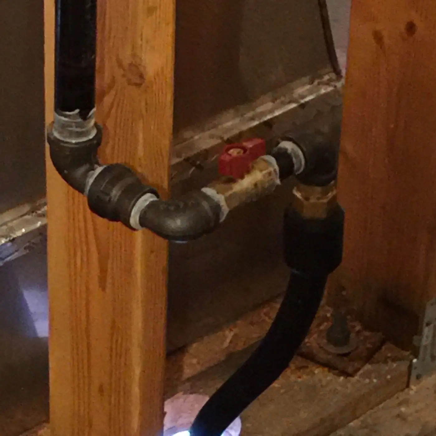 Black iron gas piping and valve running along a wood post