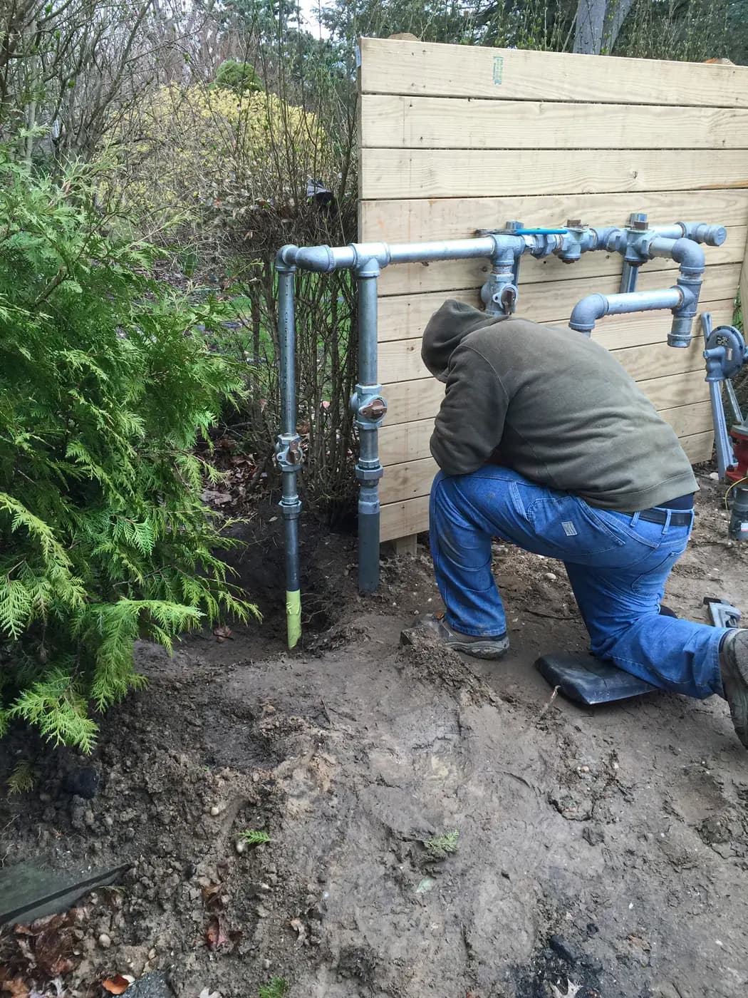 Worker assembling galvanized pipe manifold on a fence outdoors
