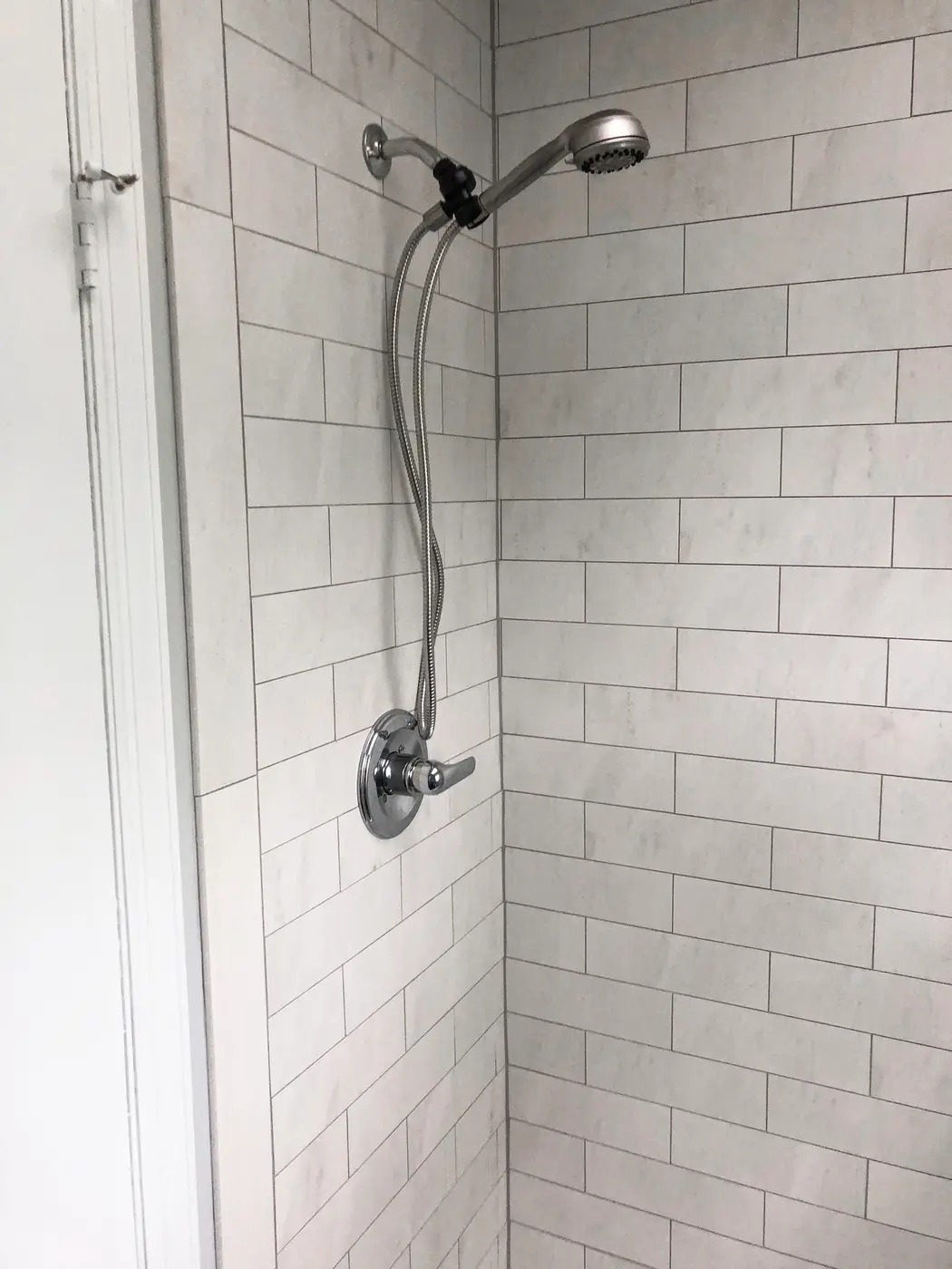 White subway tile shower with chrome showerhead and glass door
