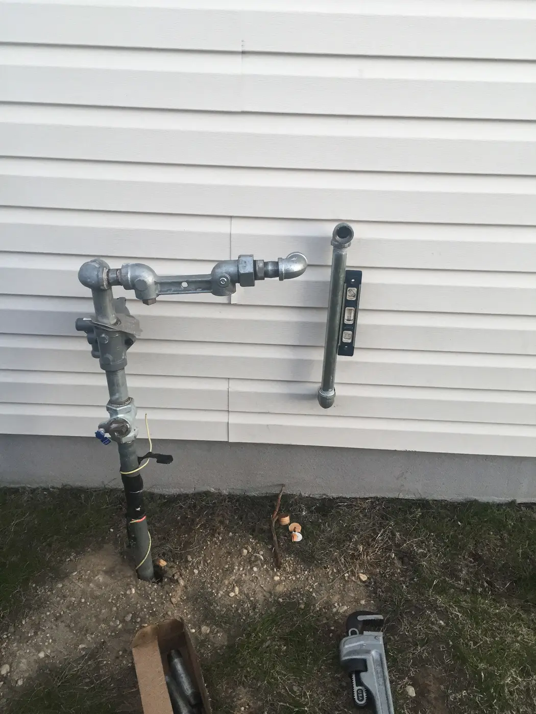 Outdoor hose bibb and backflow assembly on siding, wrench below