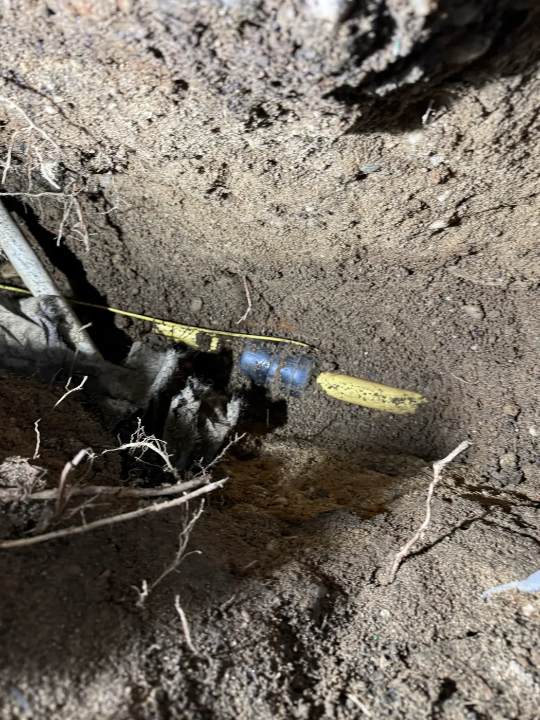 Close view of pipe fitting and yellow warning tape in dark trench