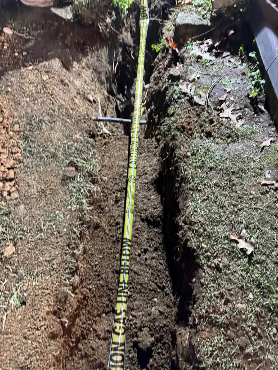 Yellow caution buried gas line tape laid along an open lawn trench