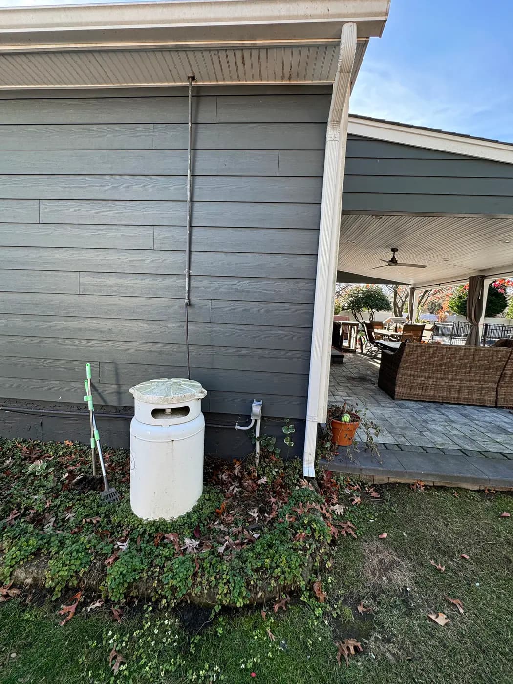 White cylindrical tank and new riser piping beside gray house near covered patio
