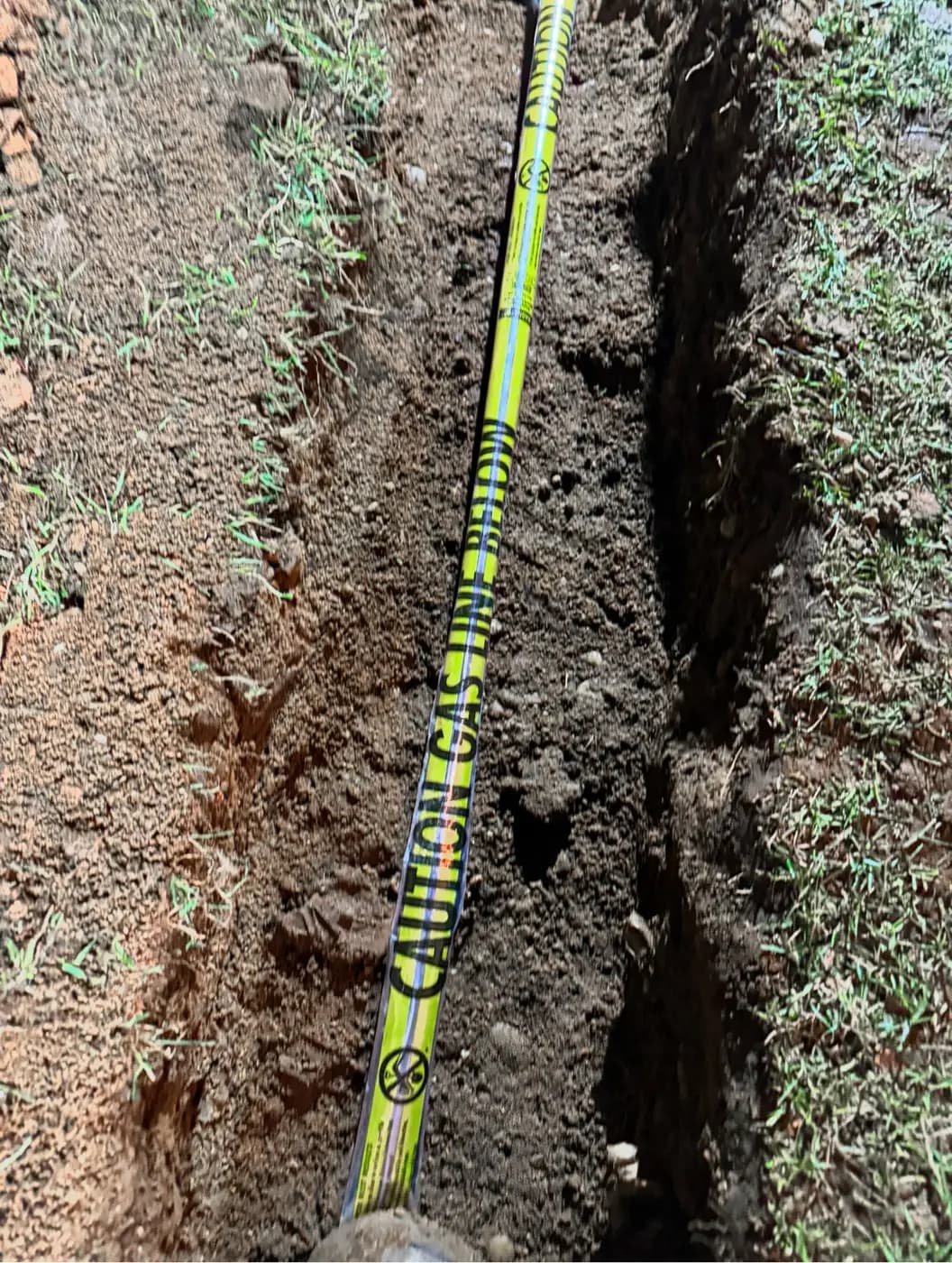 Yellow caution buried gas line tape running the length of a trench