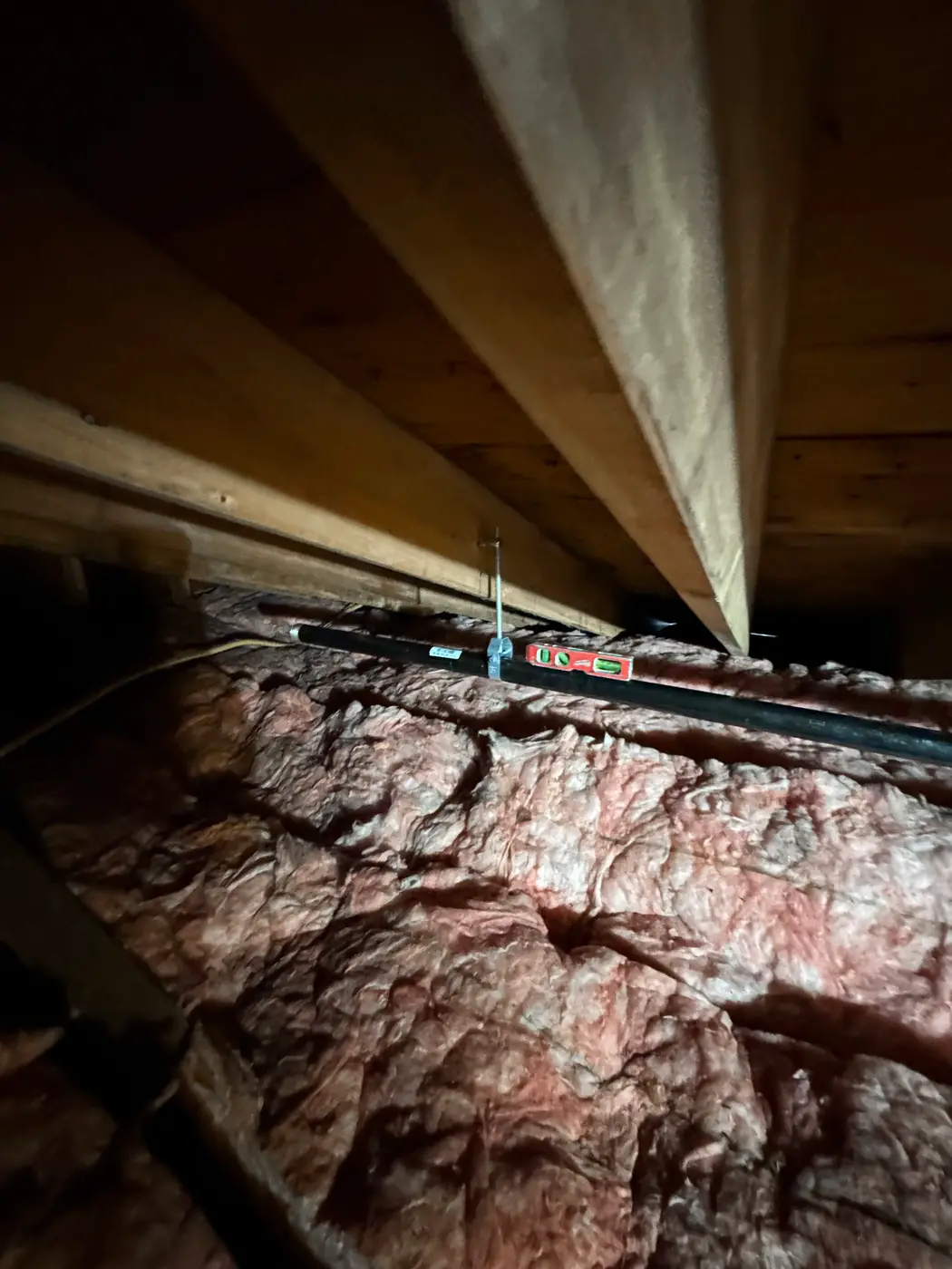 Black gas pipe run through attic framing above pink fiberglass insulation
