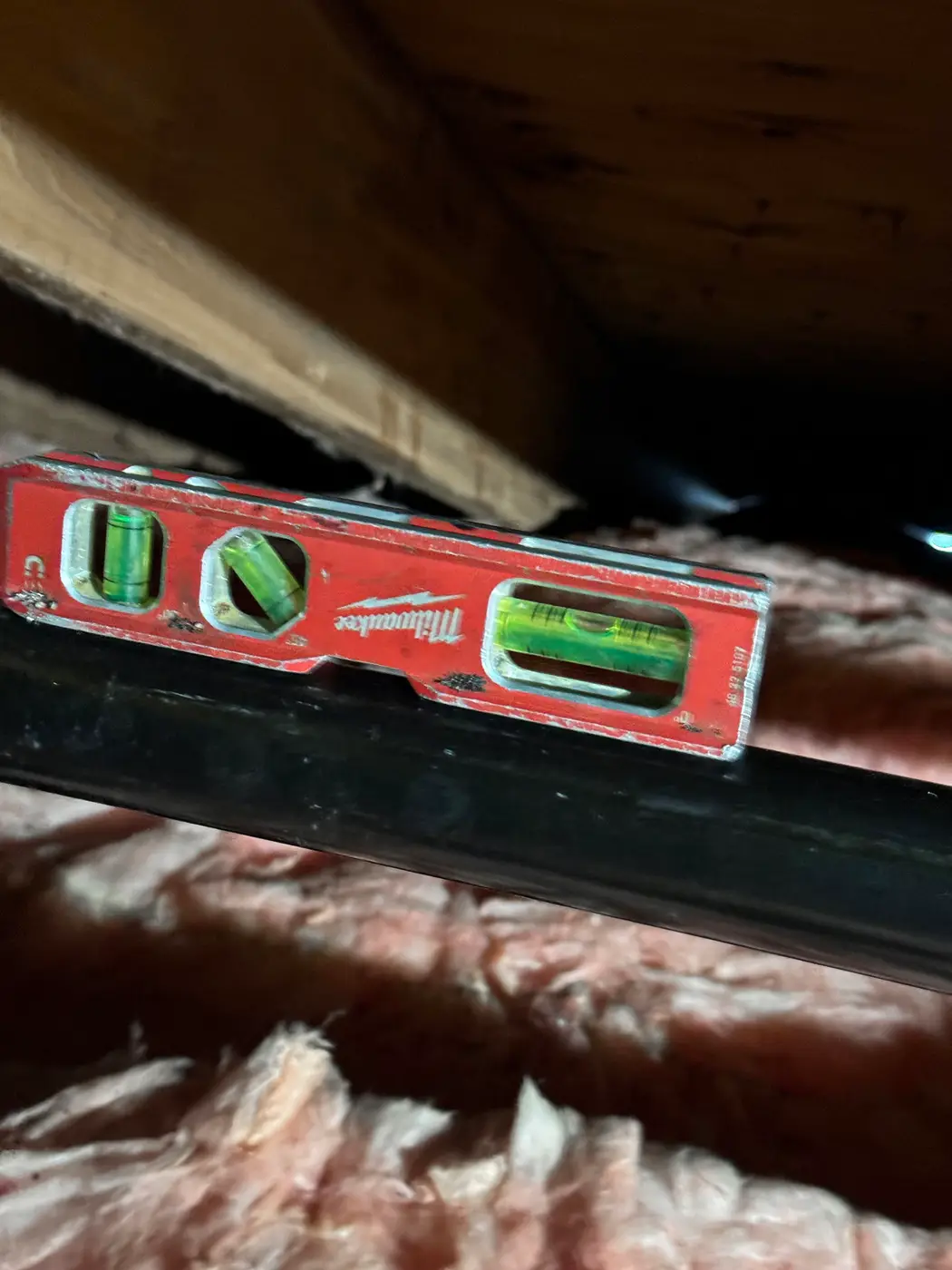 Milwaukee level set on black gas pipe running above attic insulation