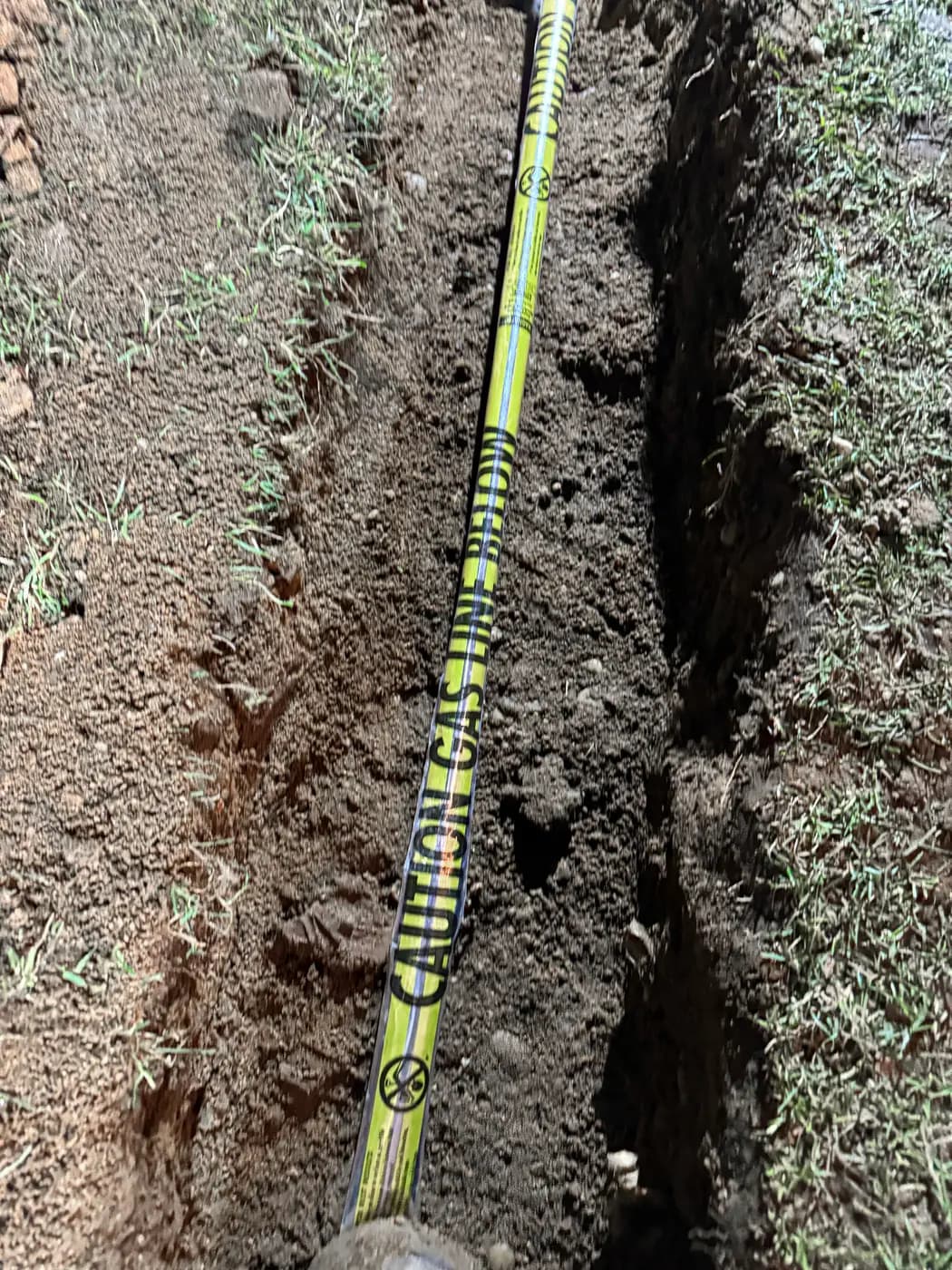 Marker tape and pipe laid in freshly dug trench across grass