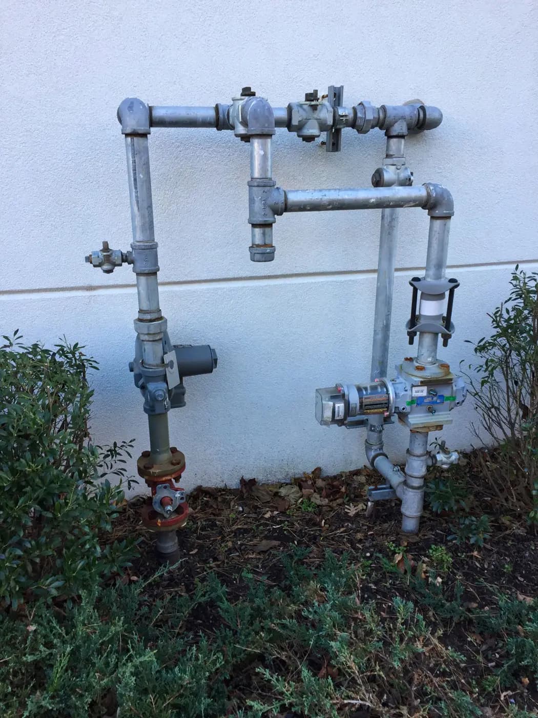 Galvanized gas manifold with multiple valves mounted on white exterior wall