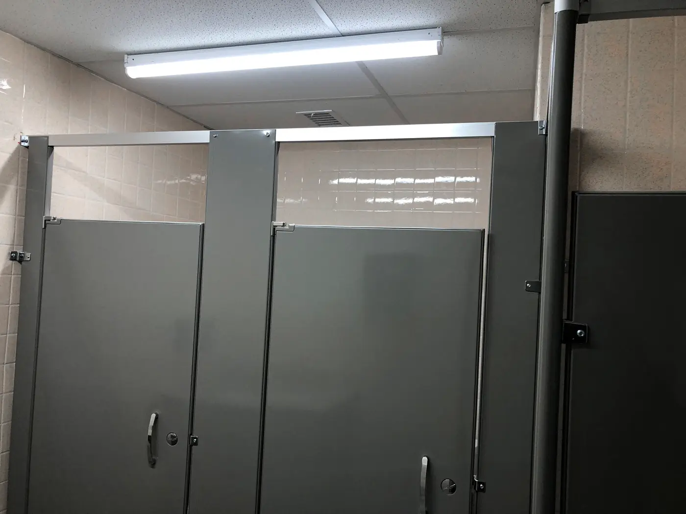 Commercial restroom with gray metal toilet partitions under fluorescent lighting